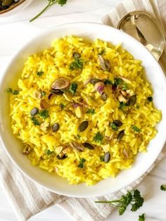 a white bowl filled with yellow rice and pistachios on top of a table