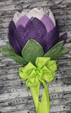 a purple and green flower on a wooden surface with a ribbon tied around the center