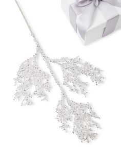 a white gift box with a silver ribbon and a decorative ornament next to it