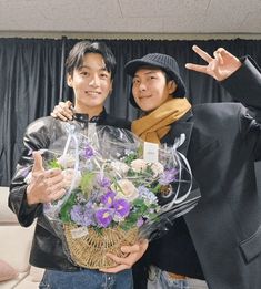 two people standing next to each other with flowers in front of them and one person giving the peace sign