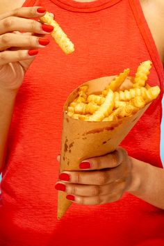 a woman in red shirt holding a paper cone filled with fried chicken strips and fries