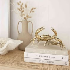 two books on a table next to a vase with flowers in it and a crab statue