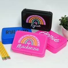 three personalized lunch boxes with pencils in front of them and a potted plant