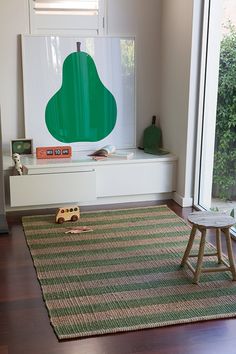 a room with a rug, toy car and green tree on the window sill