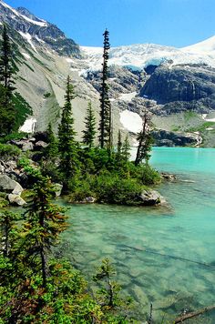 a lake surrounded by mountains and trees with snow on the mountain tops in the distance