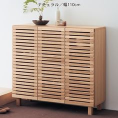 a wooden cabinet sitting on top of a floor next to a plant in a vase