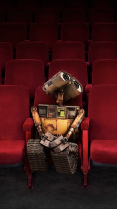 a robot sitting on top of a red chair in front of an empty theater seat