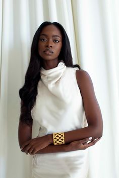 a woman in a white dress with a gold bracelet on her wrist and arms crossed