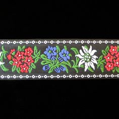 an embroidered ribbon with flowers and leaves on black background, showing the design in different colors