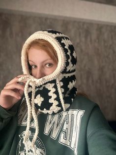 a woman with red hair wearing a black and white knitted hoodie while holding her hands to her face