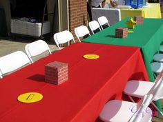 a red table topped with white chairs next to a green table covered in yellow and red cloths