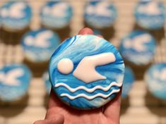 a hand holding a blue cupcake with white icing