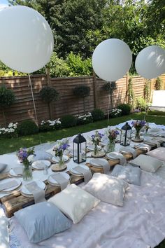 an outdoor table set up with white balloons and place settings for the guests to eat