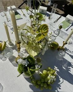 a table topped with lots of white flowers and green plants next to candlesticks