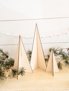 three folded paper christmas trees sitting on top of a wooden table next to pine cones