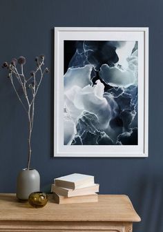 a vase with some flowers and books on a table next to a framed photograph in a room