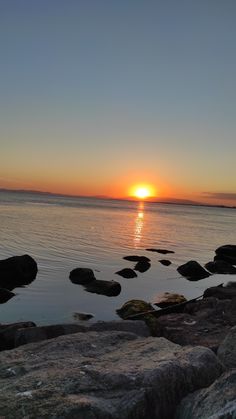 the sun is setting over the water and rocks