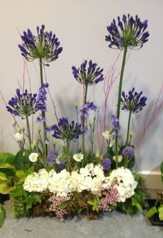 purple and white flowers are in the center of a flower arrangement with greenery around it