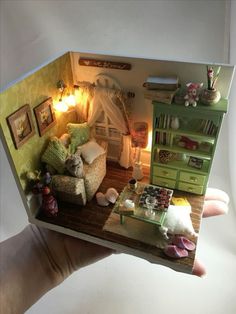 a hand holding a doll house with furniture and lights in the living room, as if it were made out of paper