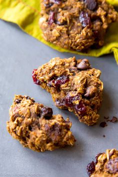 three cookies with cranberries and chocolate chips on a sheet of baking paper next to each other