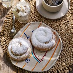 two powdered donuts on a plate next to a cup of coffee and spoon