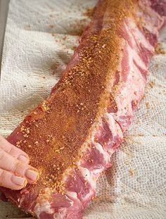 a person holding up a piece of meat on top of a white paper towel with seasoning sprinkles