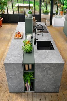 an outdoor kitchen with concrete counter tops and green plants in the center, surrounded by potted plants