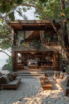 an outdoor living area with couches, tables and chairs on the sand near trees