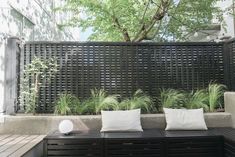 a wooden bench sitting next to a black fence with white pillows on top of it