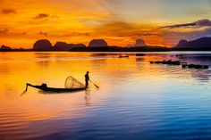 a man standing on top of a boat in the middle of water with mountains in the background