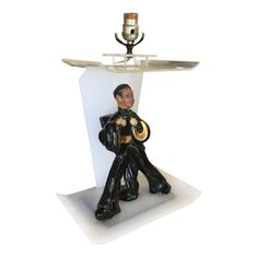 a figurine of a man sitting on top of a table with a lamp in the background