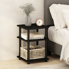 a nightstand with books and a clock on it next to a bed in a bedroom