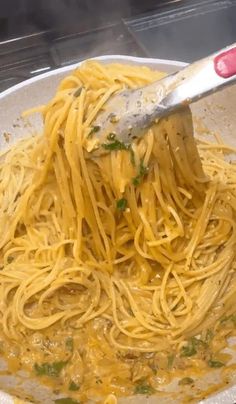 a spoon full of spaghetti being stirred with parmesan cheese and parsley in a white bowl