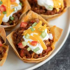 several taco shells on a plate topped with cheese and sour cream toppings,