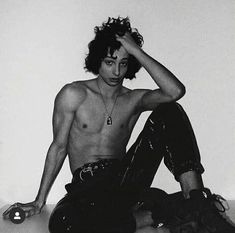 a shirtless man sitting on the floor with his hands in his hair and shoes