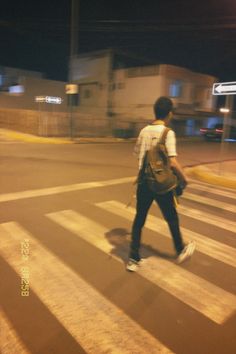 a man walking across a street at night with a backpack on his back and one foot in the air