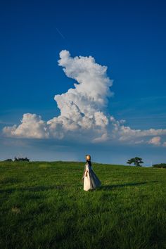 a woman is walking in the grass under a cloud