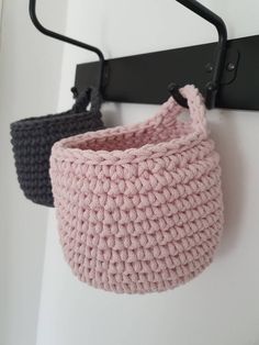 two crocheted baskets hanging from a hook on a white wall next to a black coat rack