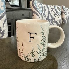 a coffee mug with the letter f on it sitting on a table next to pillows