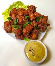 a white plate topped with chicken wings next to a bowl of mustard and green leafy garnish