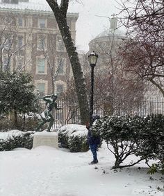 a person standing in the snow next to a lamp post and tree with lots of snow on it