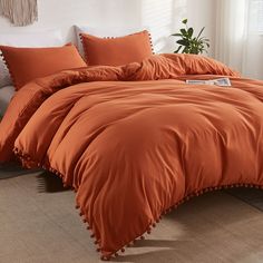 an orange comforter is in front of a white bed with pillows and a potted plant