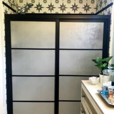 a bathroom with a walk in shower next to a white counter top and wall paper