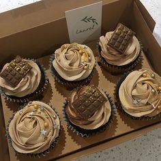 six cupcakes in a box with chocolate frosting and gold decorations on top