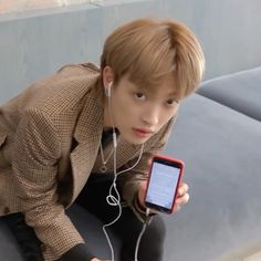 a boy with headphones is looking at his cell phone while sitting on the couch