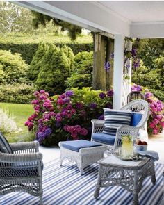 an outdoor patio with wicker furniture and flowers on the side wall, along with blue and white striped rugs