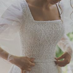 a woman in a white wedding dress is holding her hand on the back of her shoulder