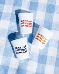 three cups that say game day are sitting on a blue and white checkered tablecloth