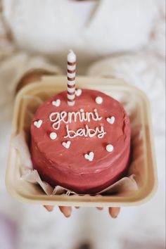 a person holding a small red cake with white frosting and a candle on top