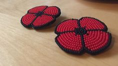 two red and black beaded buttons sitting on top of a wooden table next to each other